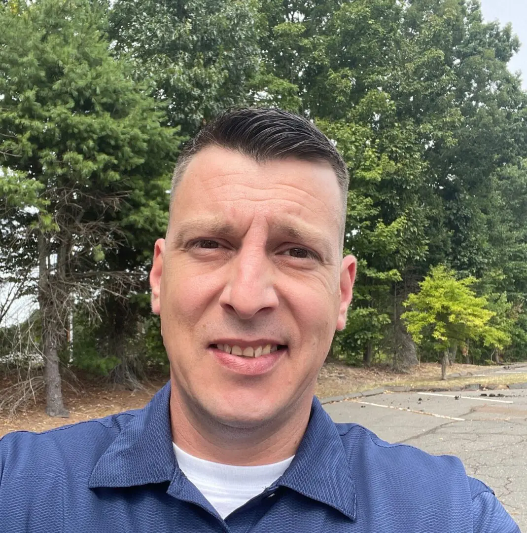 A man in blue shirt standing next to trees.